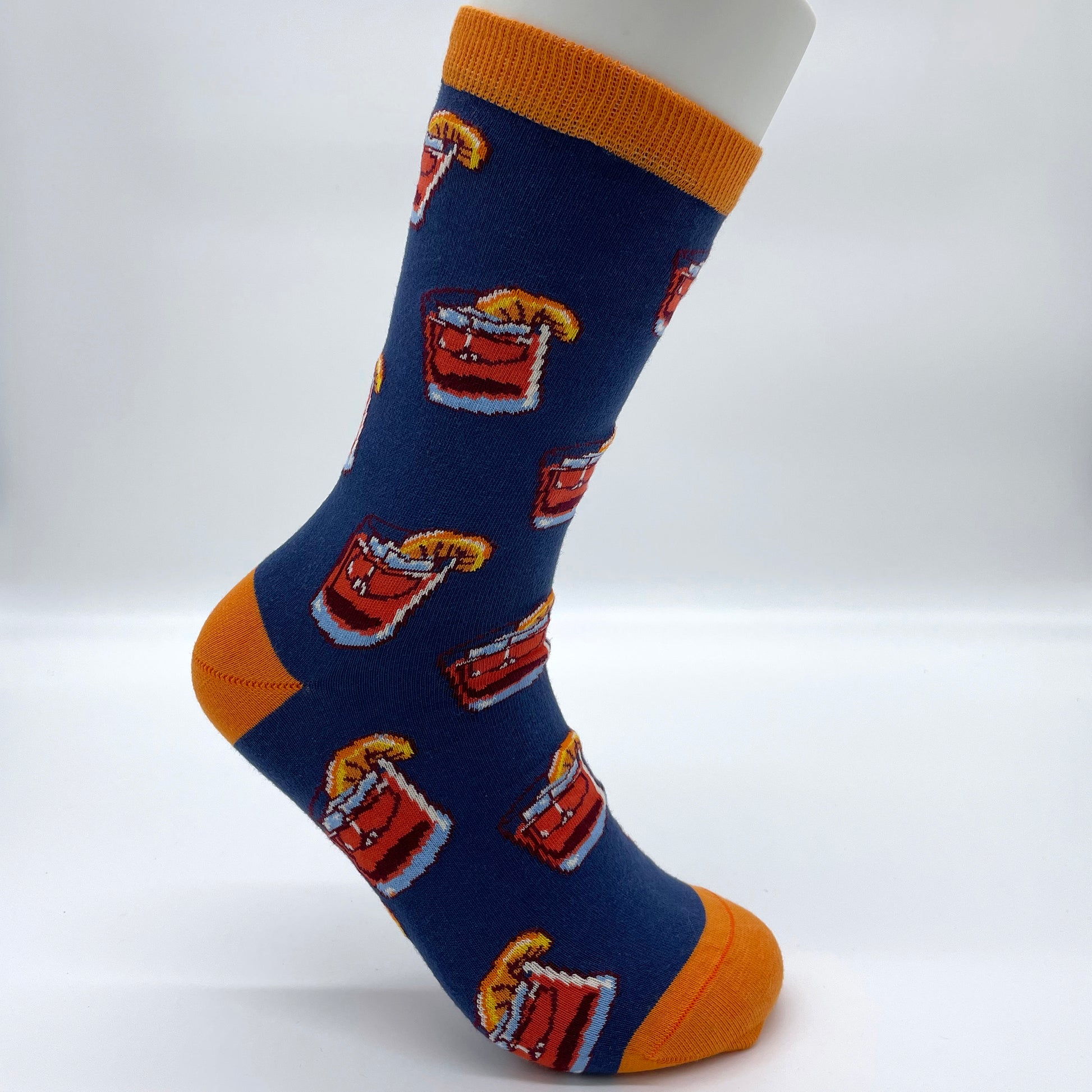 A white sock mannequin sports a blue sock patterned with glasses full of negronis. The welt, heel and toe is in orange.
