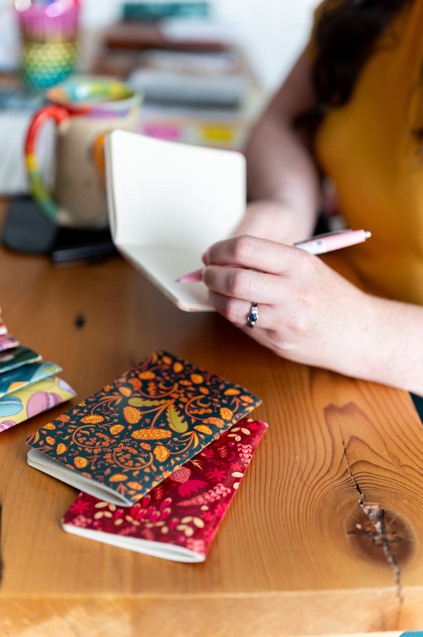 A person holds a dot grid pocket notebook open with a pen poised above it. Around it are several other pocket notebooks.