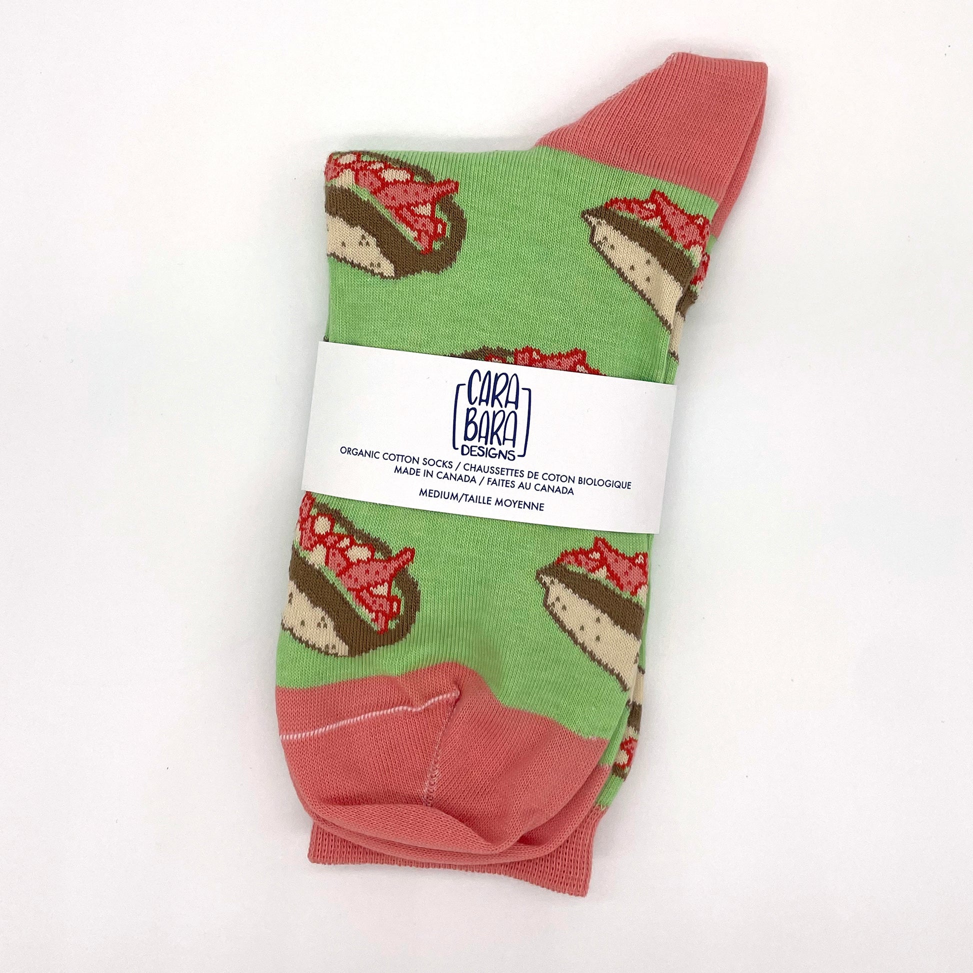 A pair of green socks patterned with lobster rolls are folded and packed with a white Carabara Designs belly band.