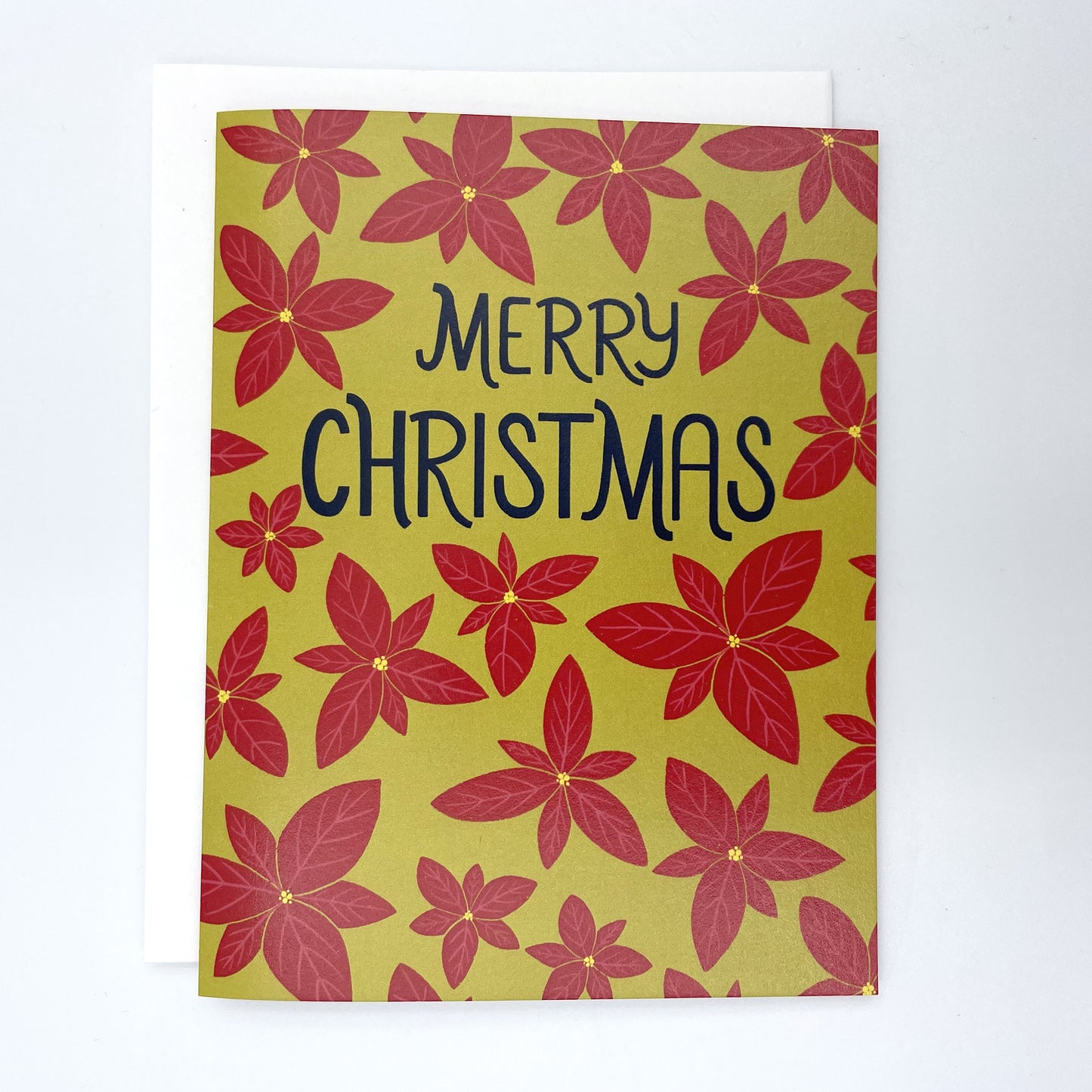 A bright green card features a pattern of bright red poinsettias and the words Merry Christmas in navy in the upper third. The card is against a white envelope on a white background.
