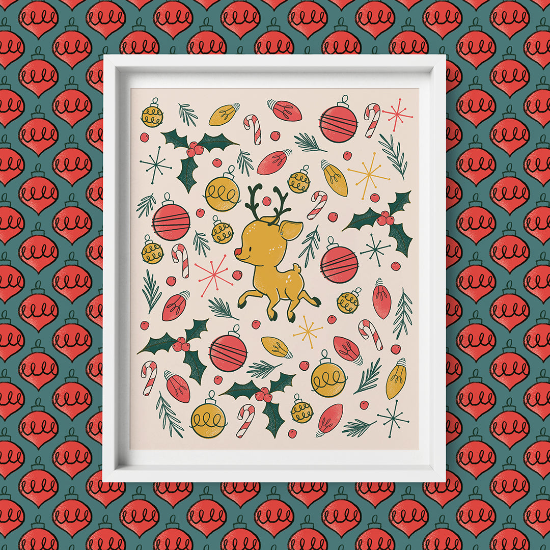 A cute reindeer is at the centre of a cluster of holly, Christmas lights, tree ornaments and greenery branches, all on a blush pink background. The print is in a white frame on a pattern of red teardrop ornaments on a blue background.