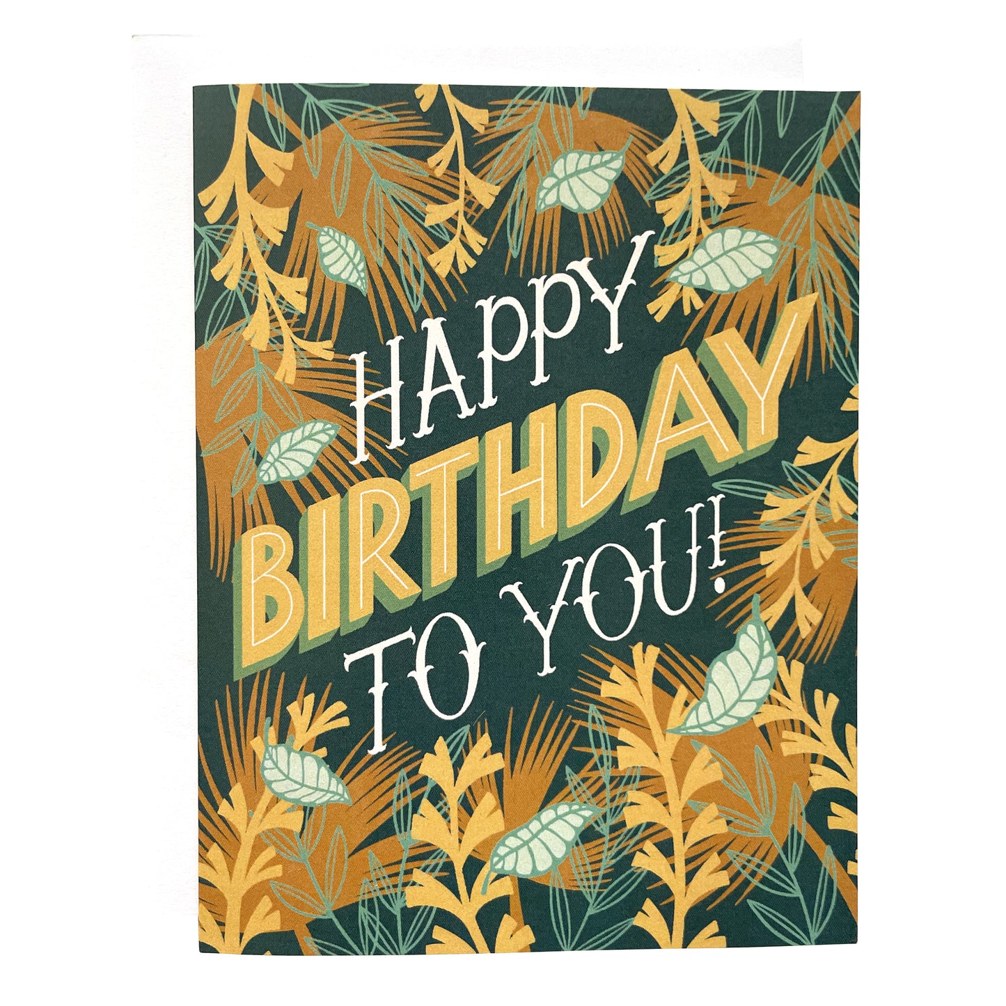 A dark blue greeting card features the hand-lettered words Happy Birthday to you! The letters are framed by illustrations of tropical leaves and vines. The card sits against a white envelope on a white background.