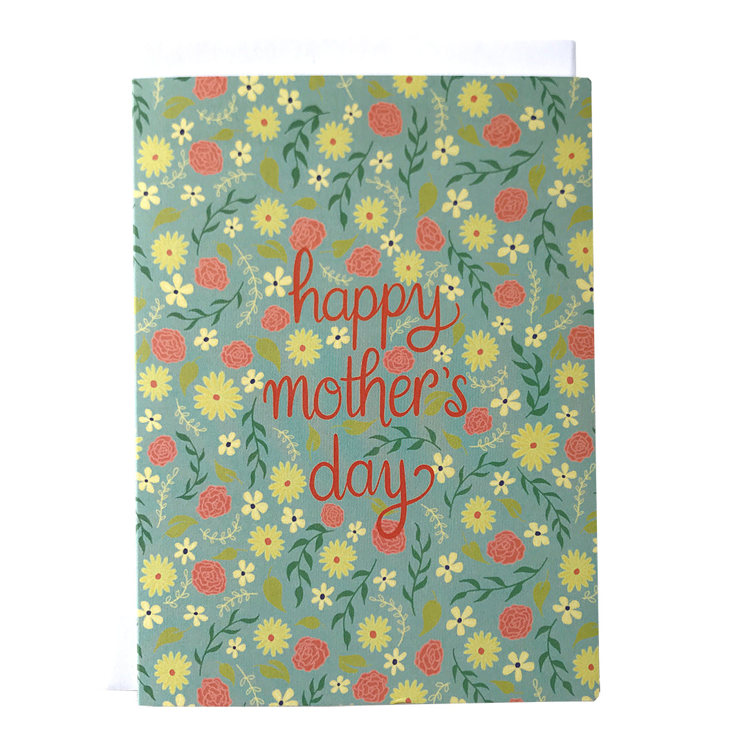 A mint-green greeting card is covered with a pattern of tiny yellow and pink flowers and the words happy mother's day in red letters. The card sits against a white envelope on a white background.