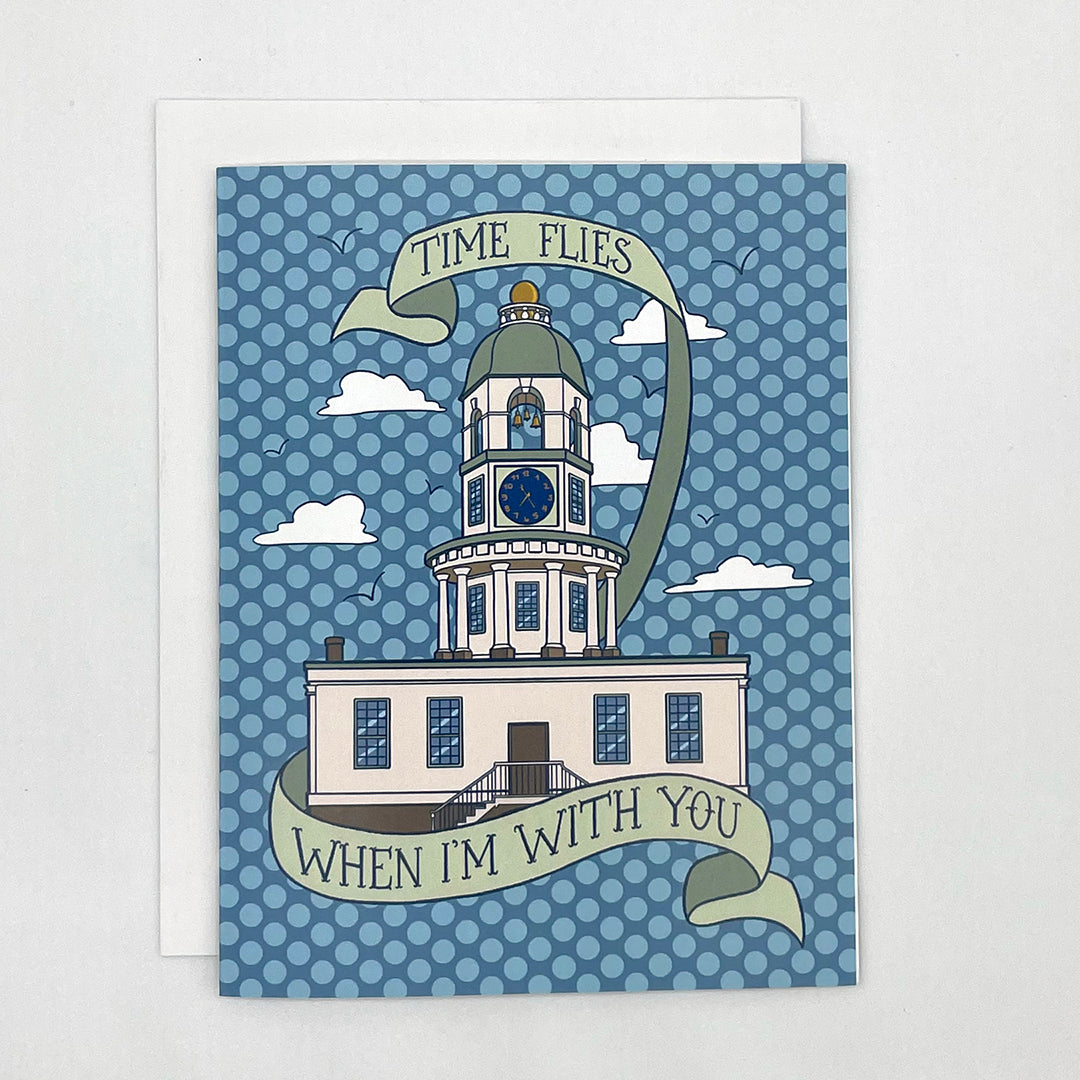 A blue polka dot greeting card features an illustration of the Halifax town clock with scattered clouds and seagulls. A hand-lettered banner reads Time Flies when I'm with You. The card is on a white envelope on a white background.
