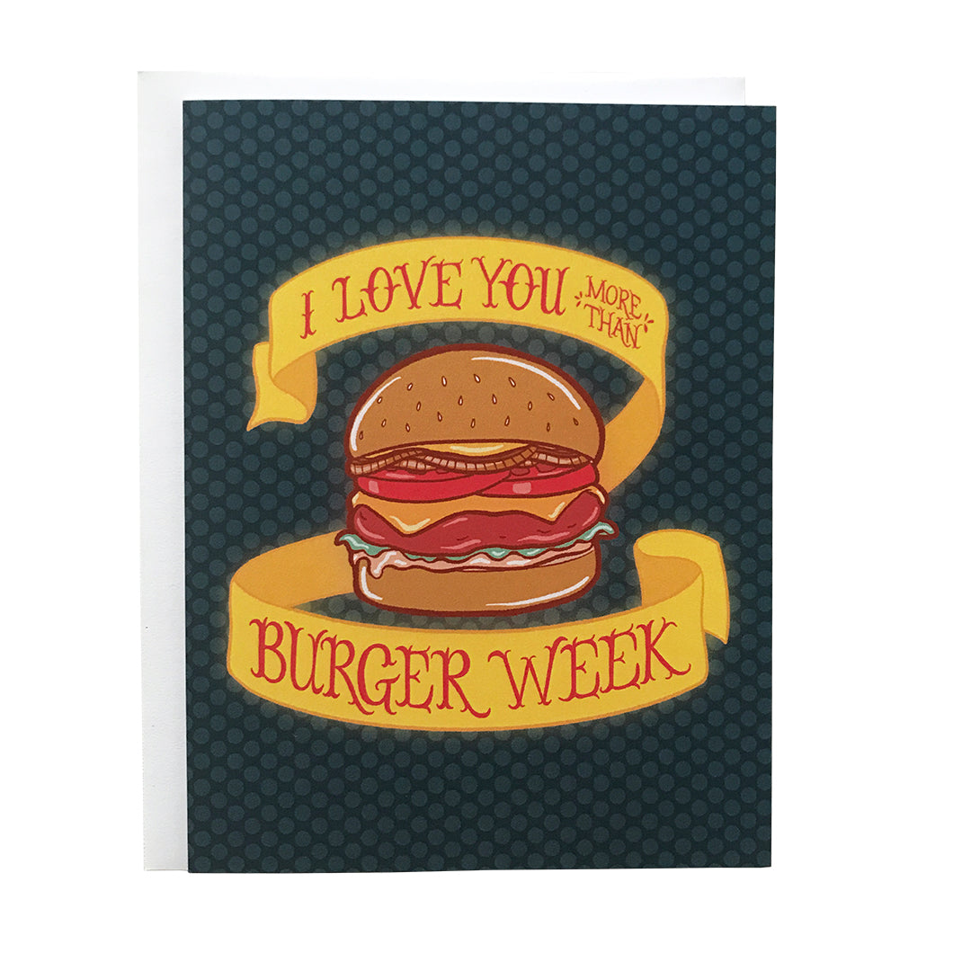 A navy greeting card features an illustration of a juicy cheeseburger along with a banner reading I love you more than burger week in red letters. The yellow banner has a slight glow to it. The card sits against a white envelope on a white background.