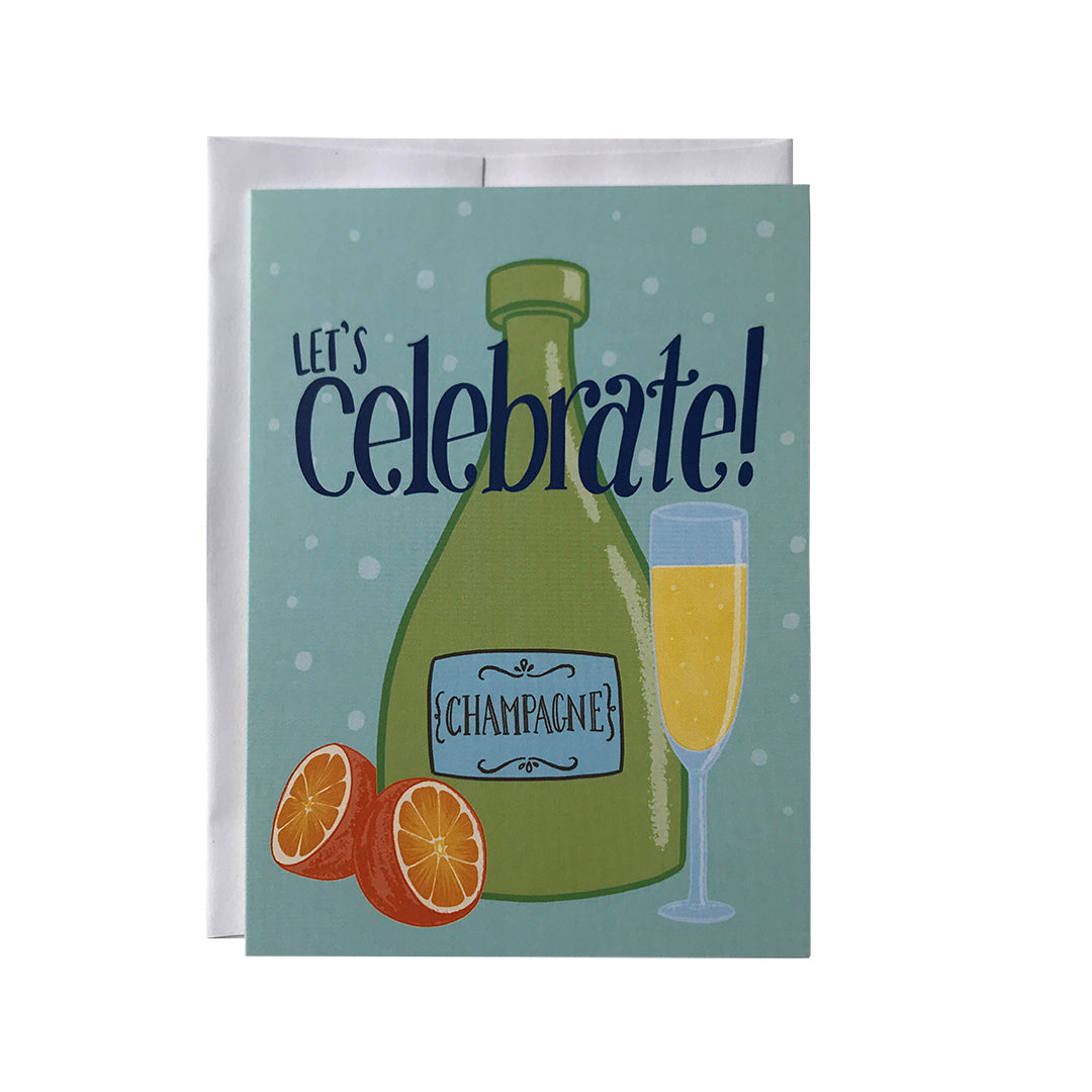 A pastel blue greeting card shows an illustration of a bottle of champagne, a halved orange and a full champagne flute. On the card are the words let's celebrate in blue lowercase letters. The card sits against a white envelope on a white background.