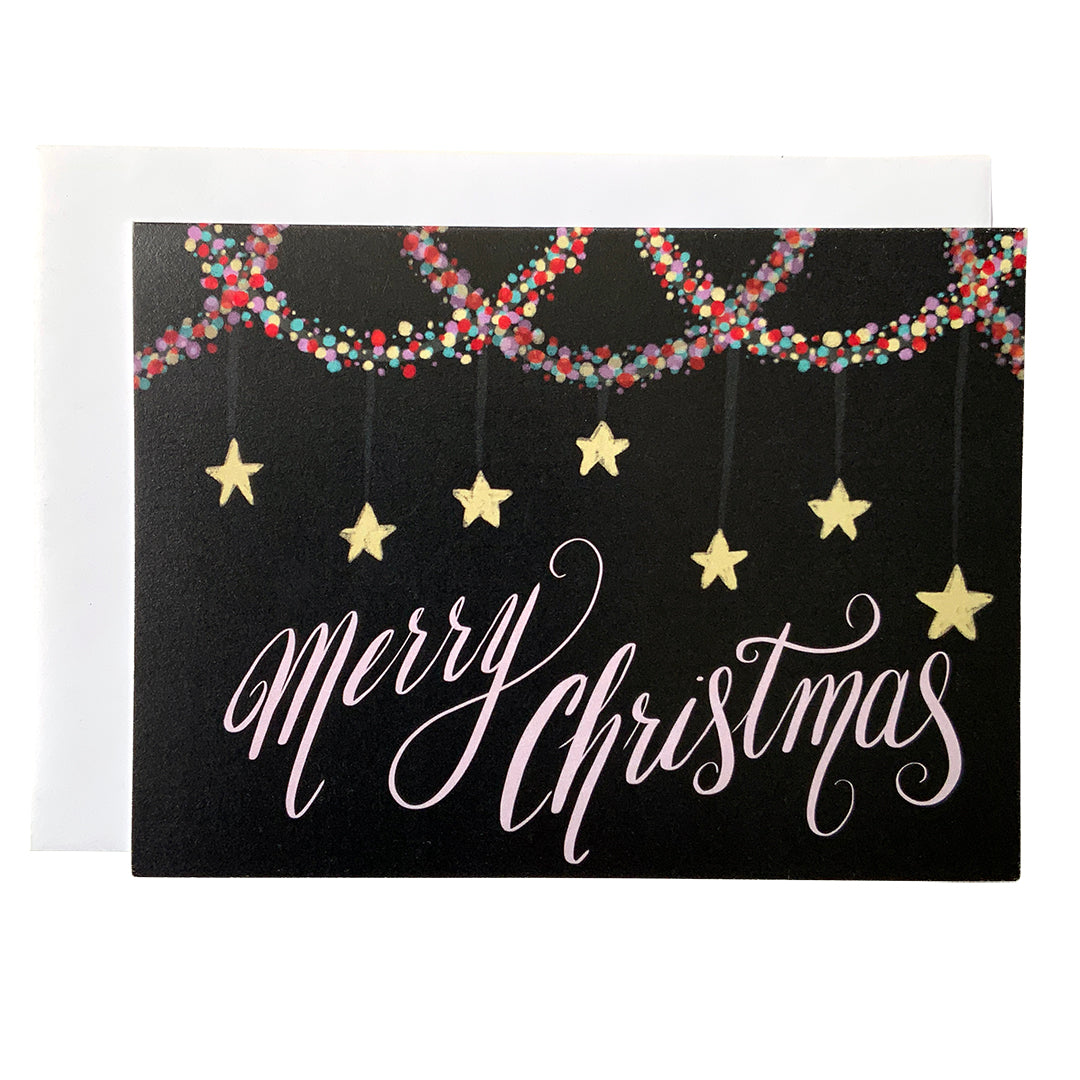A black landscape-oriented greeting card shows the words Merry Christmas in pale pink with multi-coloured garland at the top and stars hanging above the words.
