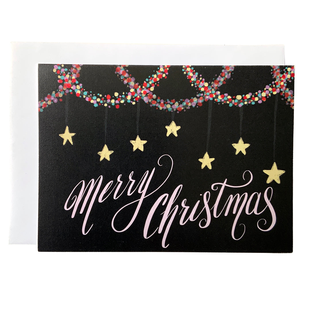 A black landscape-oriented greeting card shows the words Merry Christmas in pale pink with multi-coloured garland at the top and stars hanging above the words. 