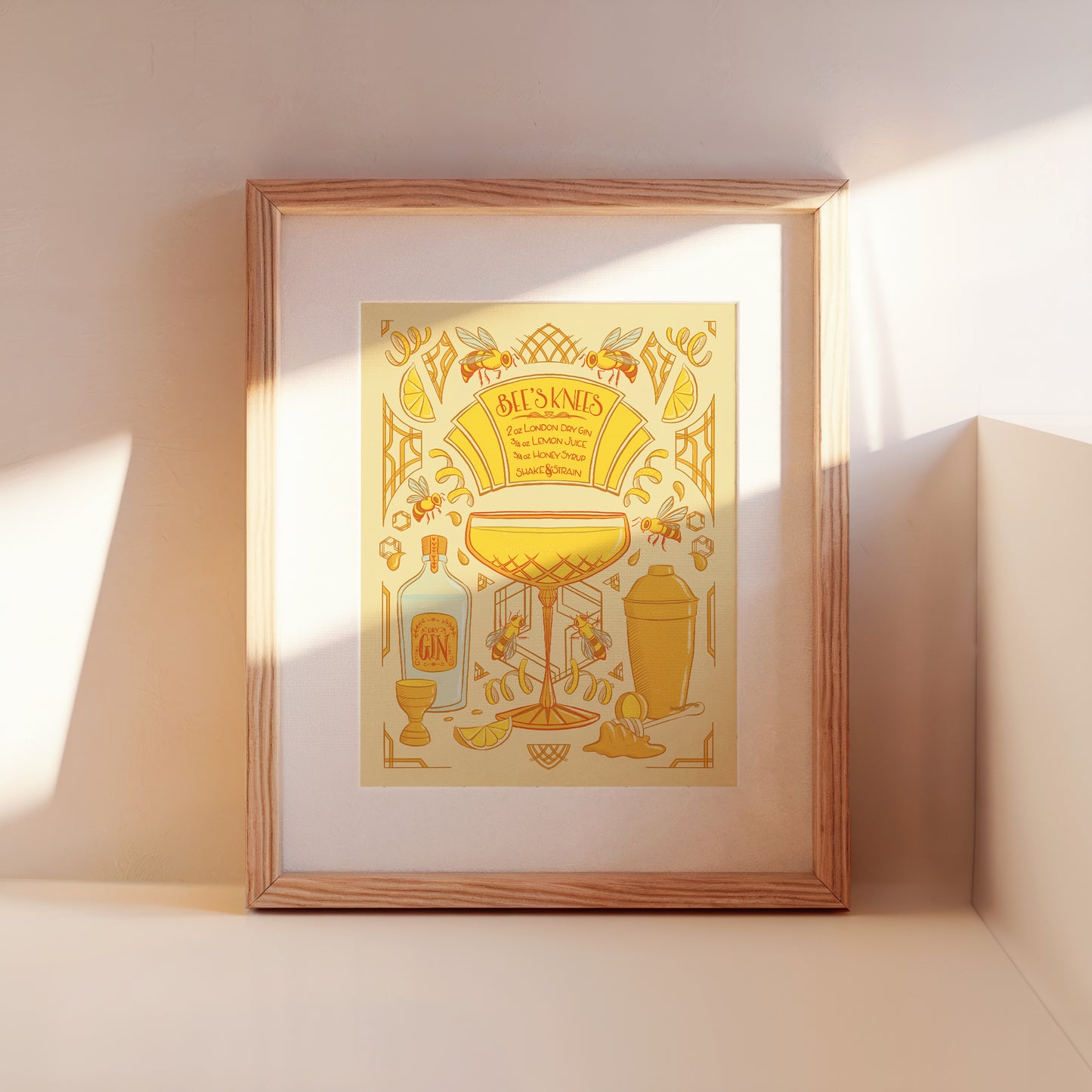 A framed Bee's Knees cocktail recipe illustration leans against a wall.