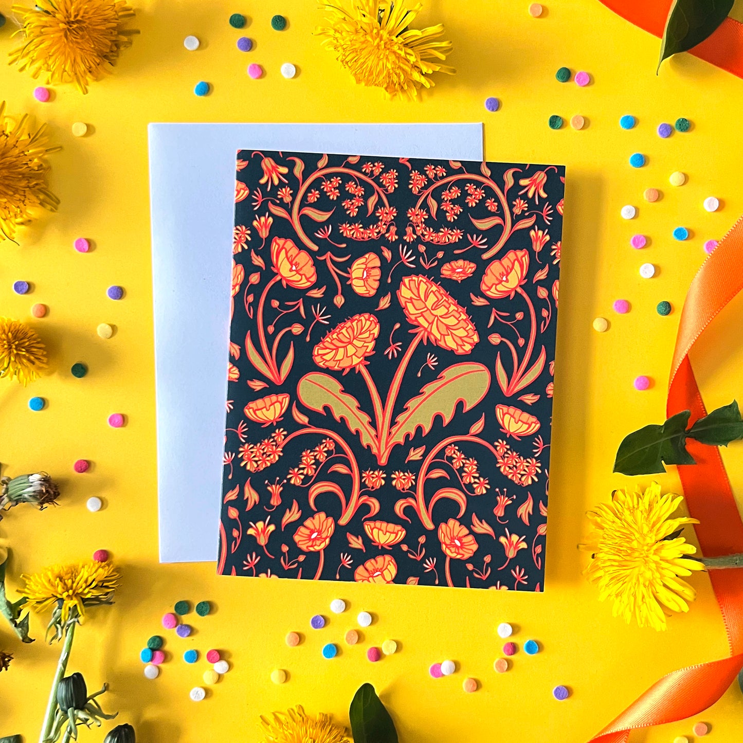 A dandelion patterned note card is on yellow with dandelions, ribbon and confetti.