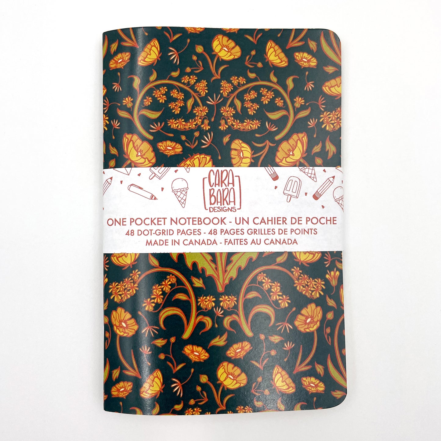 A small closed notebook has a cover patterned with dandelions, buttercups and goldenrod. The notebook is bound with a Carabara Designs belly band indicating in both French and English that it is a pocket notebook containing 48 dot grid pages and is made in Canada.