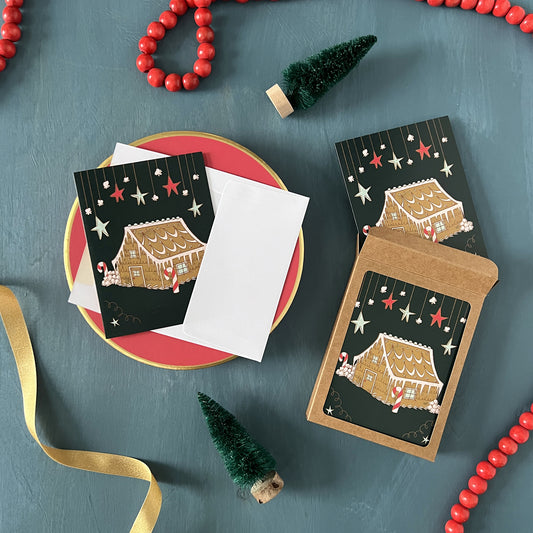 Christmas greeting cards with gingerbread houses appear on a festive blue background with red beads, green ribbon, and bottle brush trees.