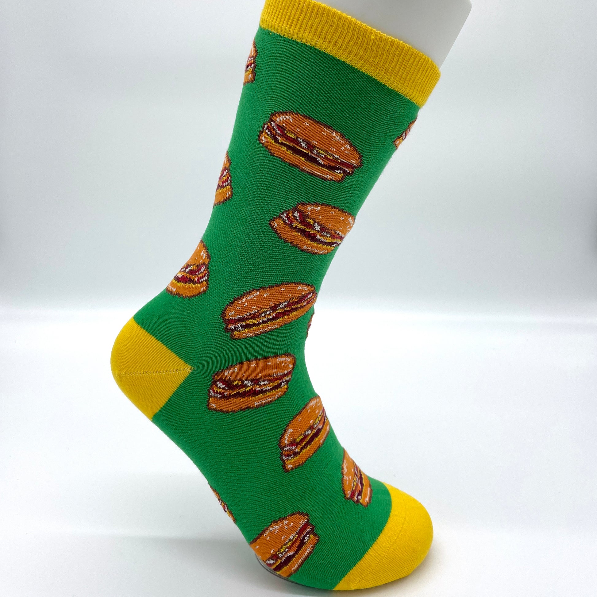 A white sock mannequin sports a green sock patterned with cheeseburgers. The welt, heel and toe are yellow.