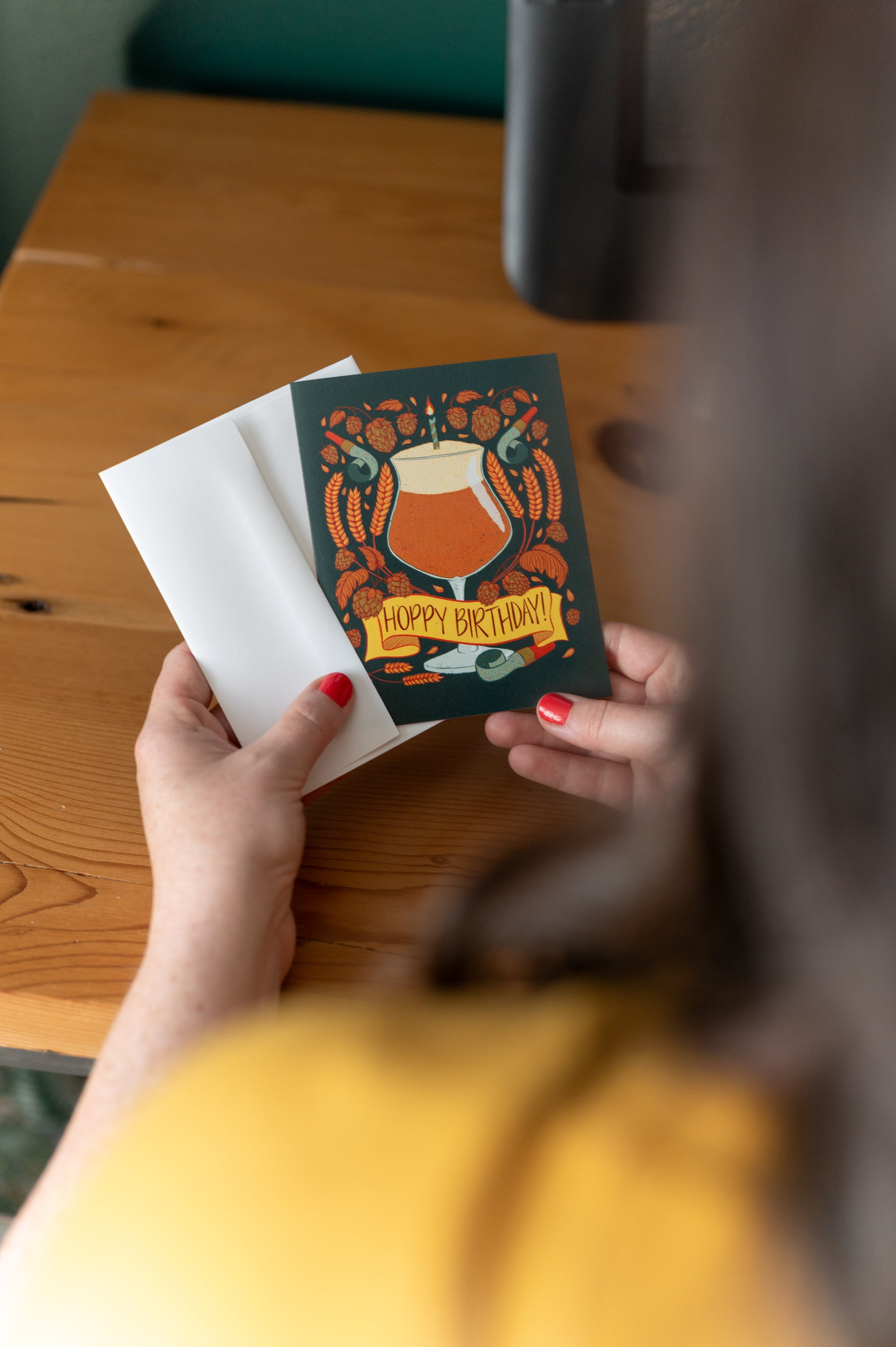 A person holds a dark green beer themed birthday card against a wooden table.