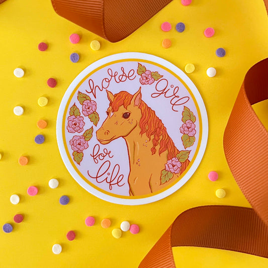 A round vinyl sticker with a horse reads Horse Girl for Life. It is on yellow with confetti and brown ribbon.