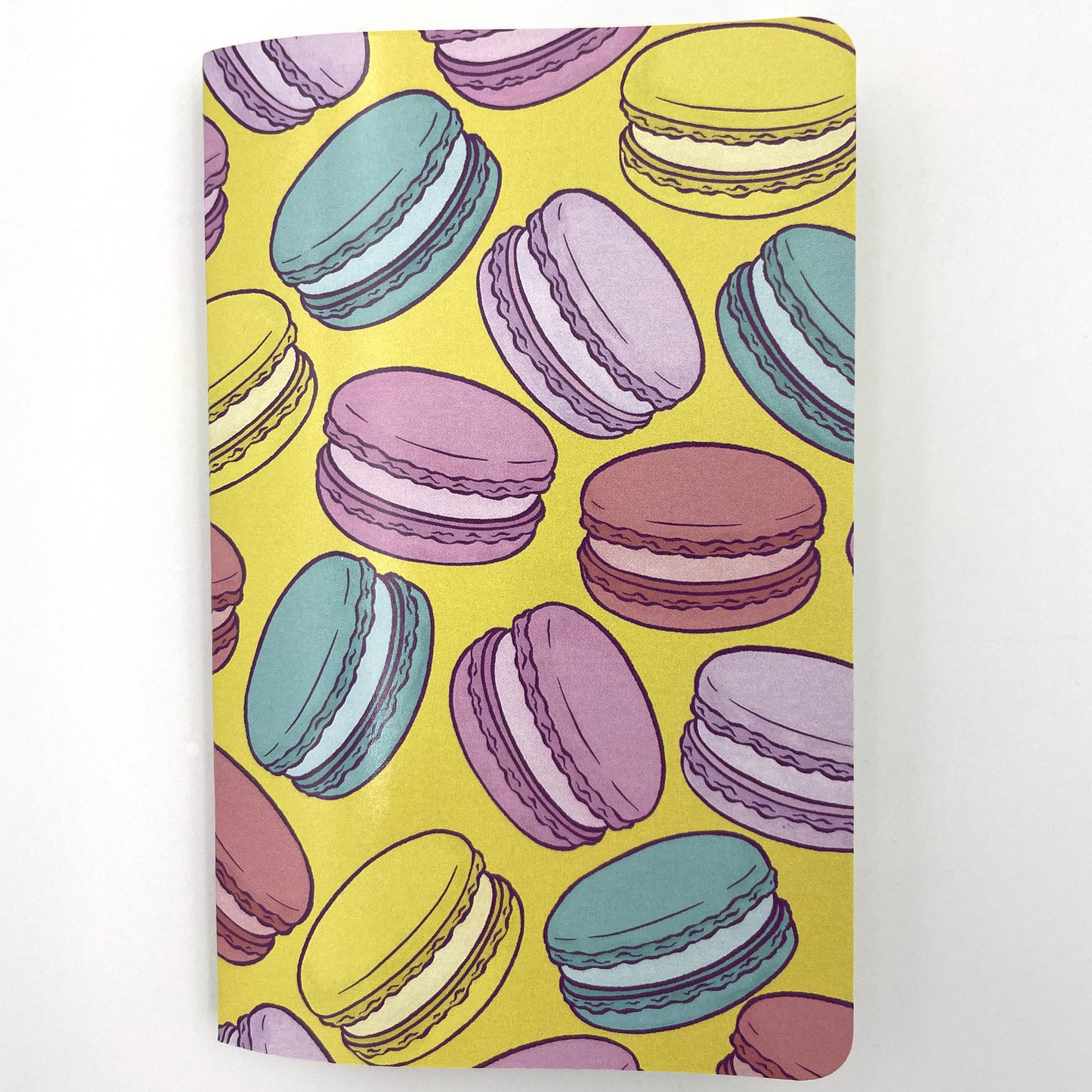 A small closed notebook has a cover that shows a rainbow of macarons against a yellow background.