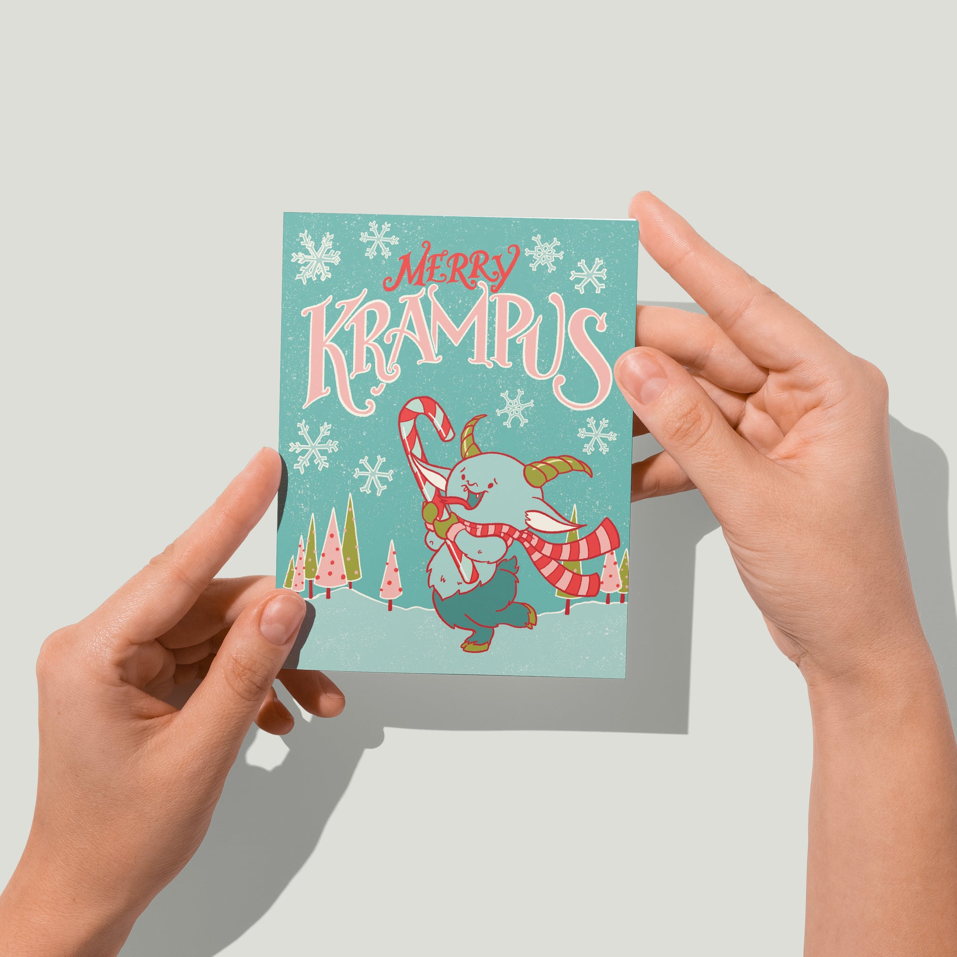 Hands hold a retro Christmas card with a cute Krampus on it up to the camera.