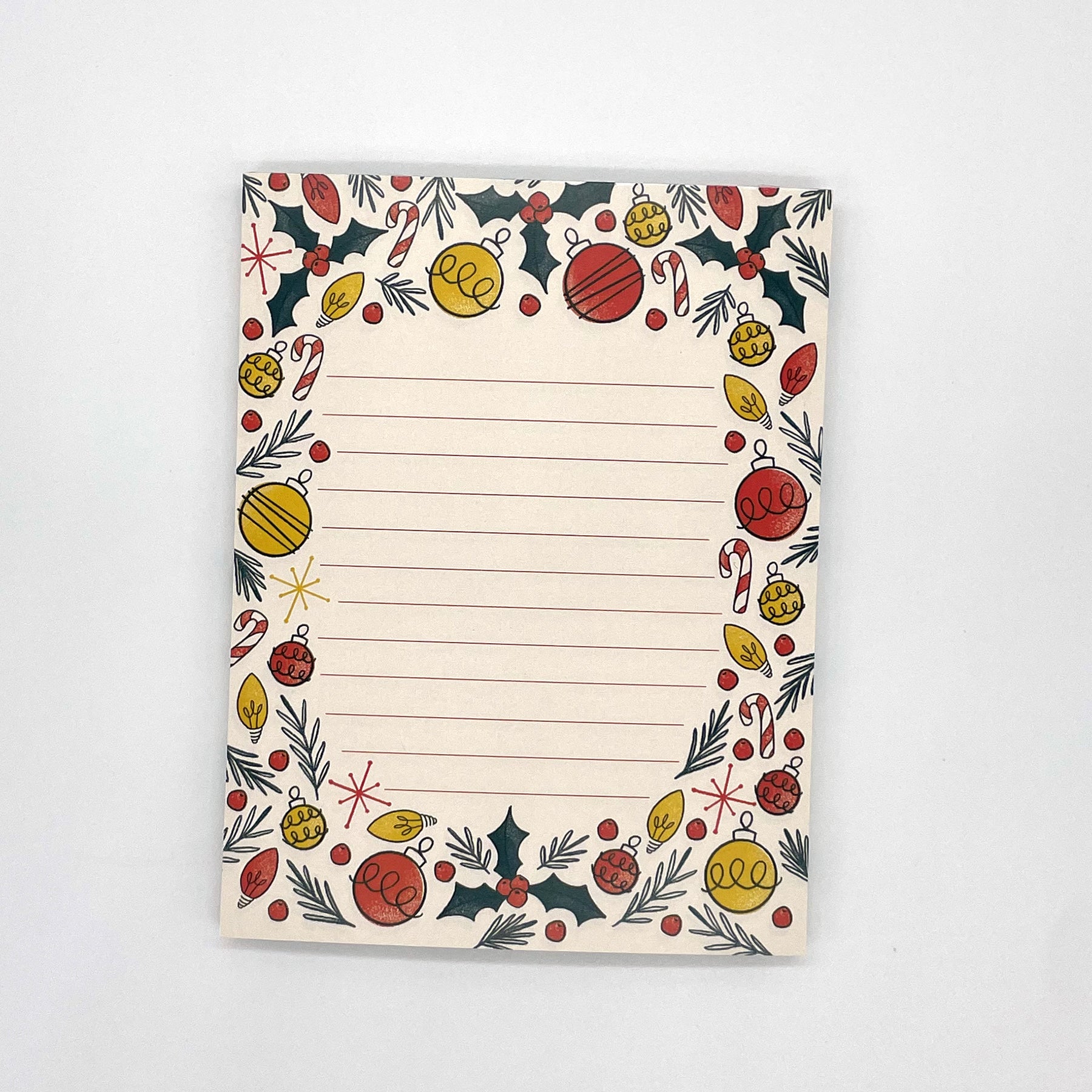 A pale peach lined notepad features illustrations of holly, ornaments, christmas lights, candy canes, and pine sprigs.