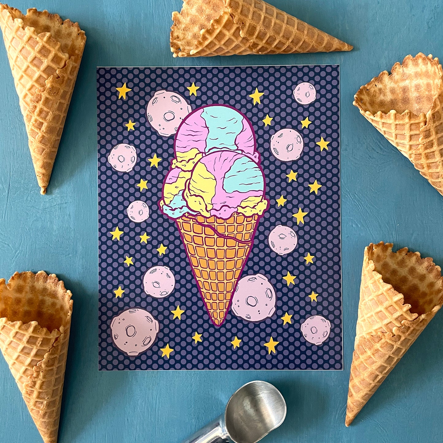 An illustration of a purple, blue, and yellow triple scoop ice cream cone is flanked by stars and moons on a purple polka dot background. The print on a blue background surrounded by waffle cones.
