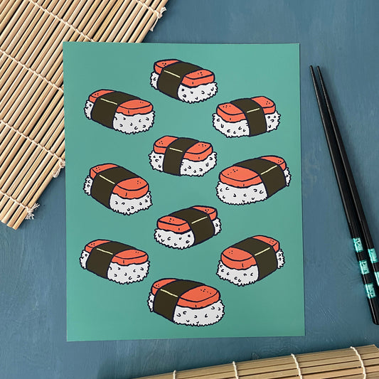 An art print shows a cluster of musubi-style sushi on a turquoise background. The art print sits on a sushi mat next to chopsticks.
