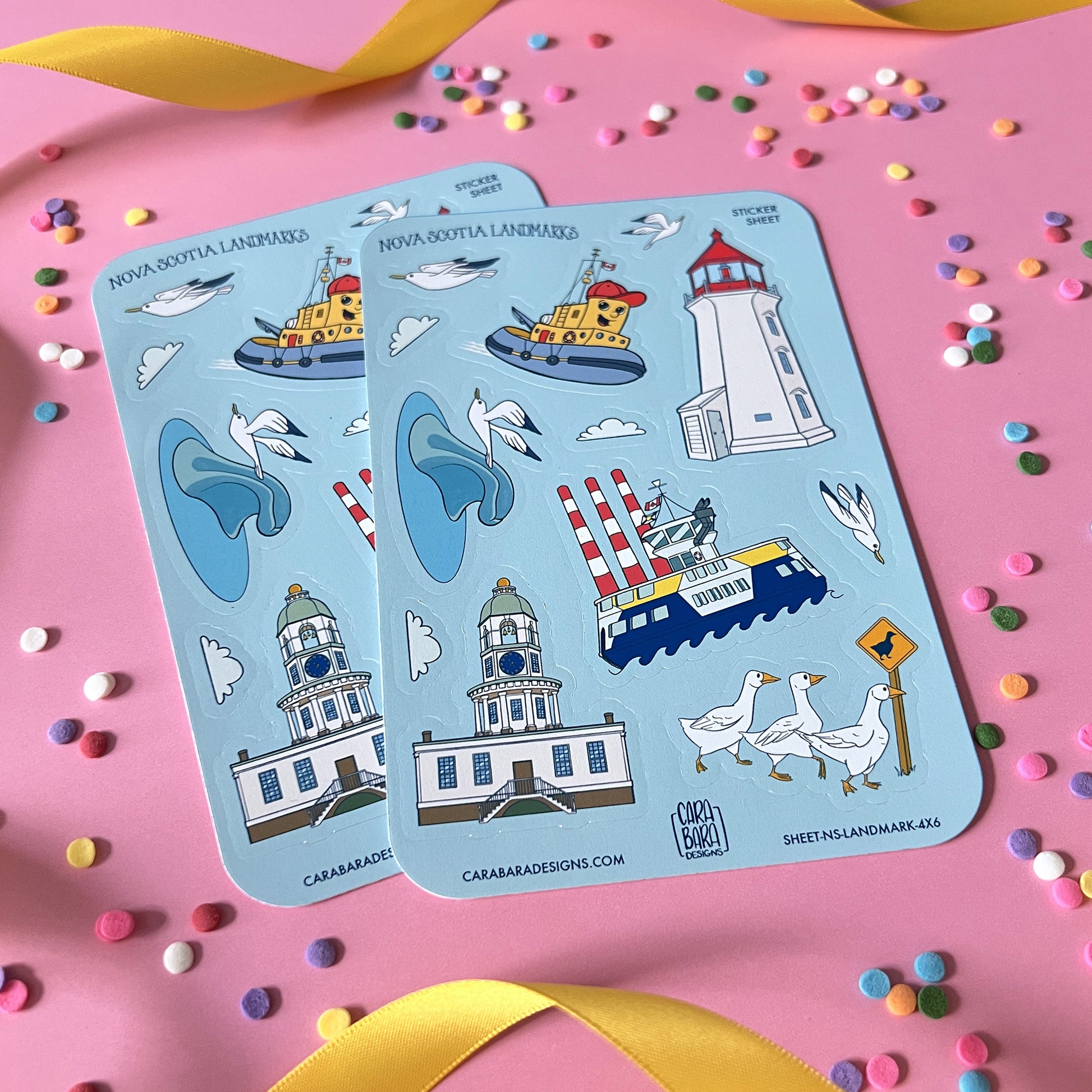 Two blue vinyl sticker sheets featuring landmarks from Halifax and in and around Nova Scotia are on a pink background with confetti and ribbon.