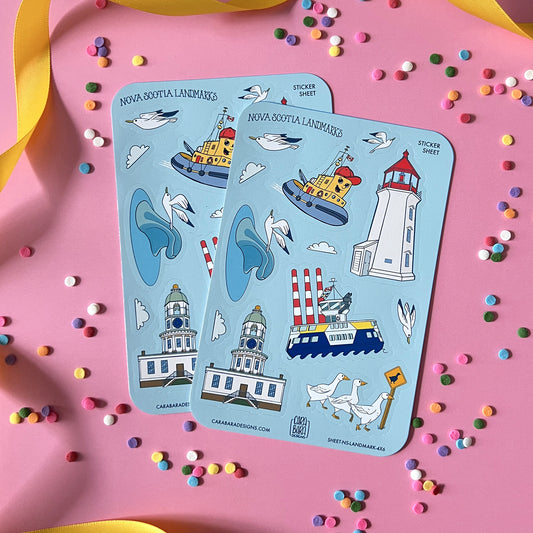 Two blue vinyl sticker sheets featuring landmarks from Halifax and in and around Nova Scotia are on a pink background with confetti and ribbon.