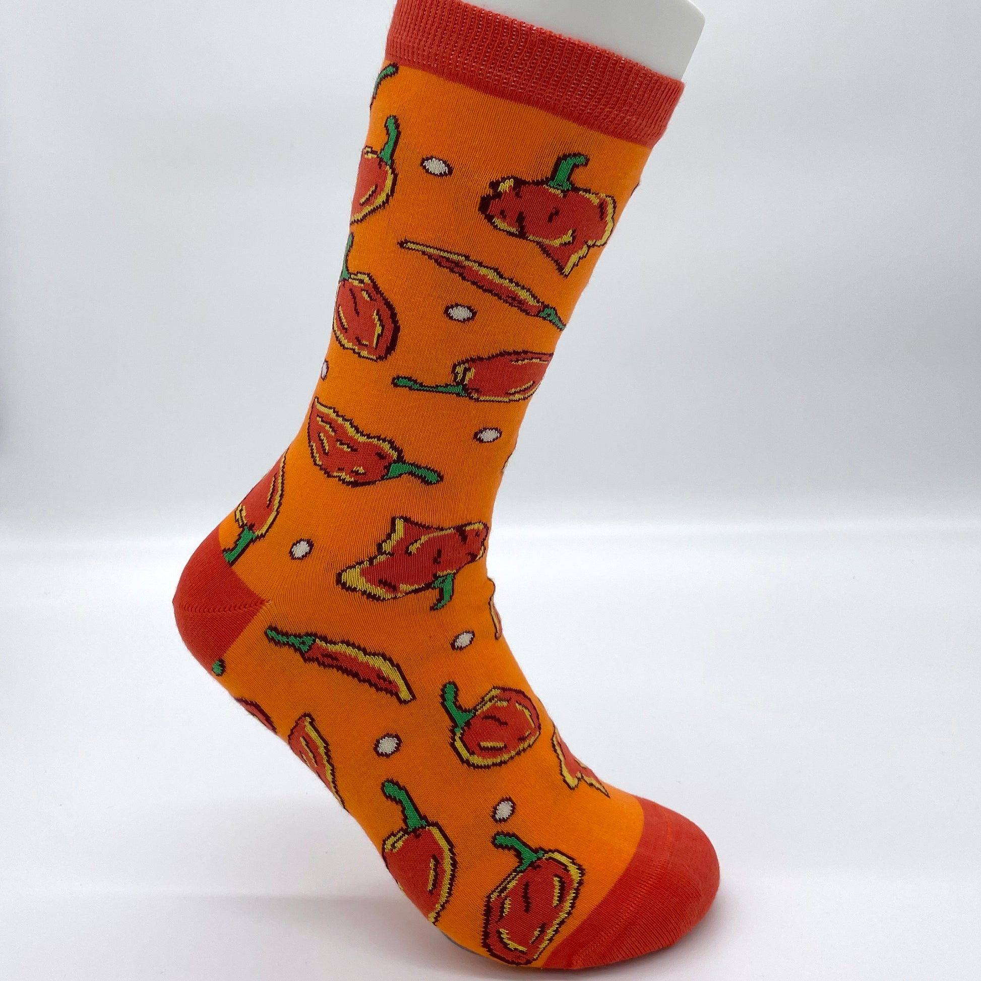 A white sock mannequin sports an orange sock patterned with a variety of spicy peppers in red. The heel, welt and toe of the sock are also red.