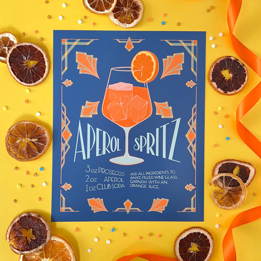 An illustrated art deco art print of a spritz cocktail is on yellow with confetti and citrus slices.