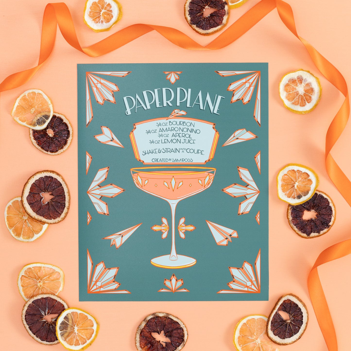 A turquoise and coral illustrated paper plane cocktail recipe is on an orange background with citrus slices and ribbon.