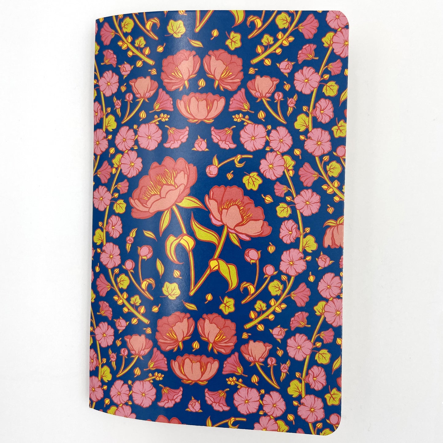 A small closed notebook has a cover that shows a pattern of pink peonies and hollyhocks on a blue background.