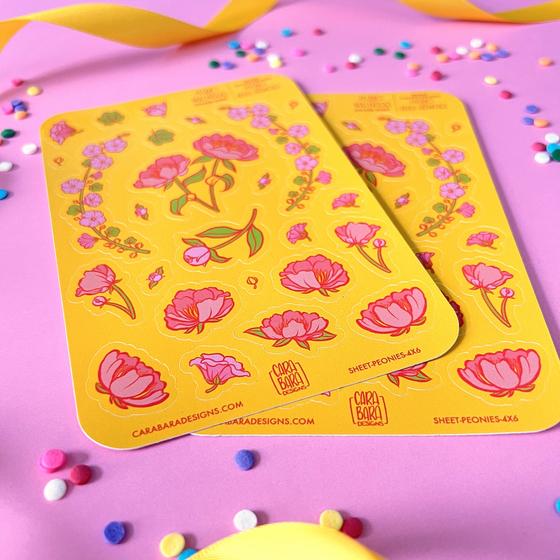 Two yellow sticker sheets featuring pink peony and pink hollyhock stickers are on a pink background with confetti and ribbon.