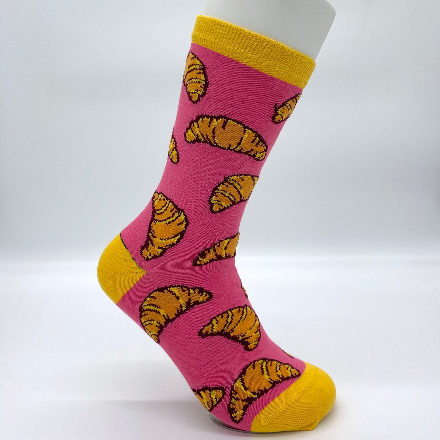 A white sock mannequin sports a pink sock patterned with croissants. The welt, heel and toe are yellow.