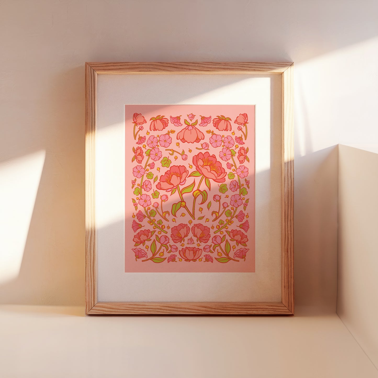 A framed art print of pink peonies on a pink background leans against a wall.