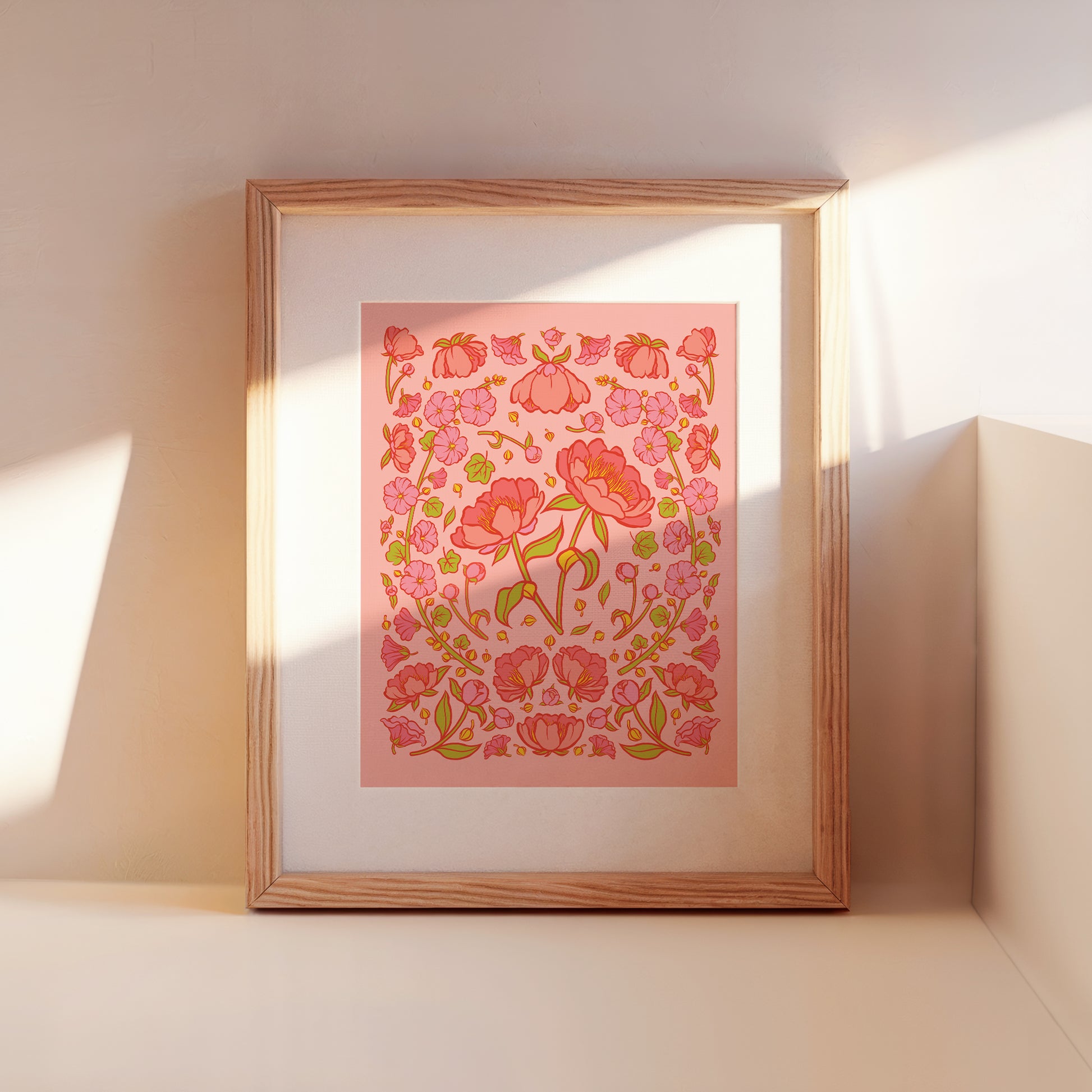 A framed art print of pink peonies on a pink background leans against a wall.