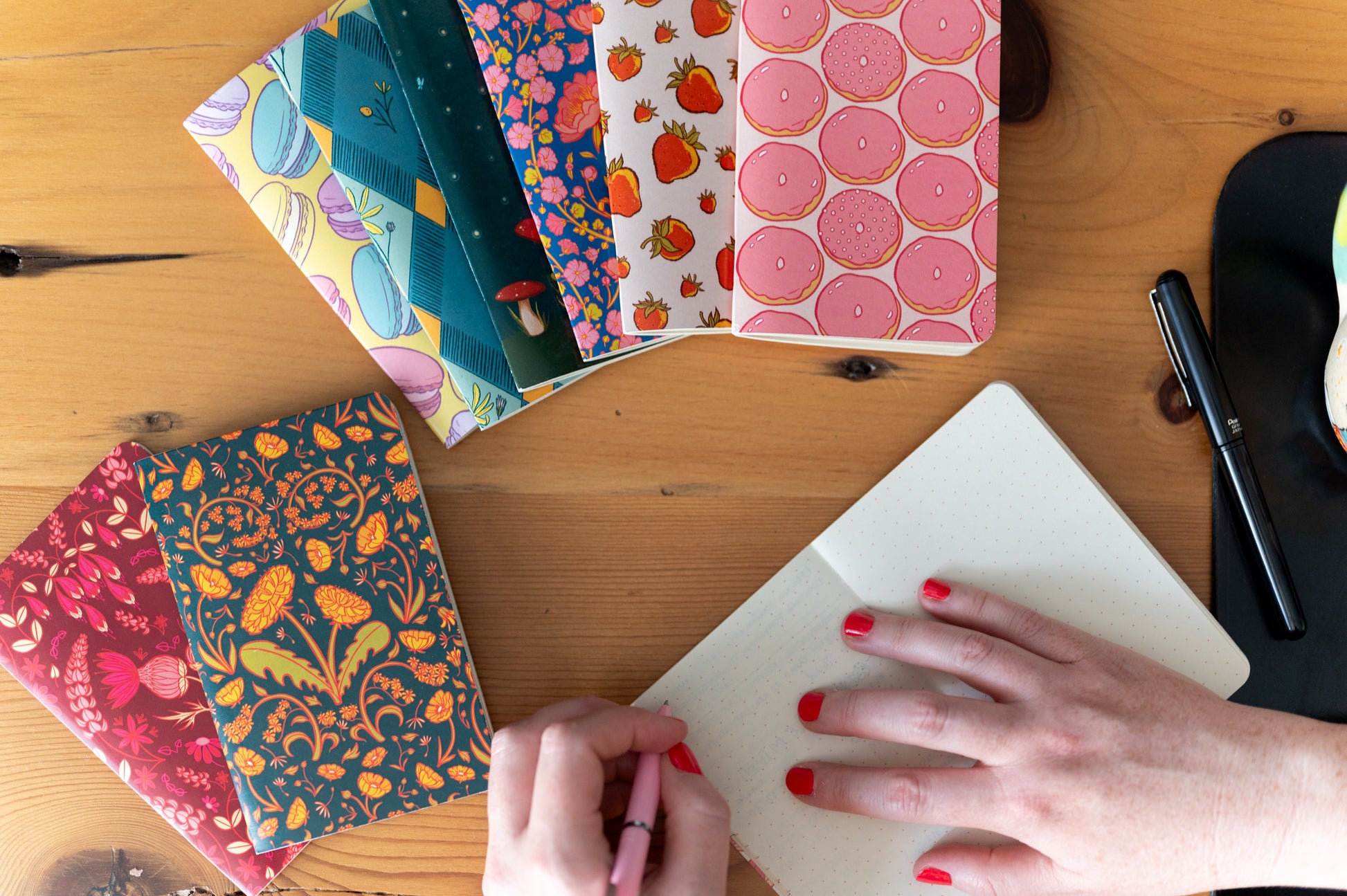 A dot grid pocket notebook is open and a person holds a pen above it. Around it are several other pocket notebooks.