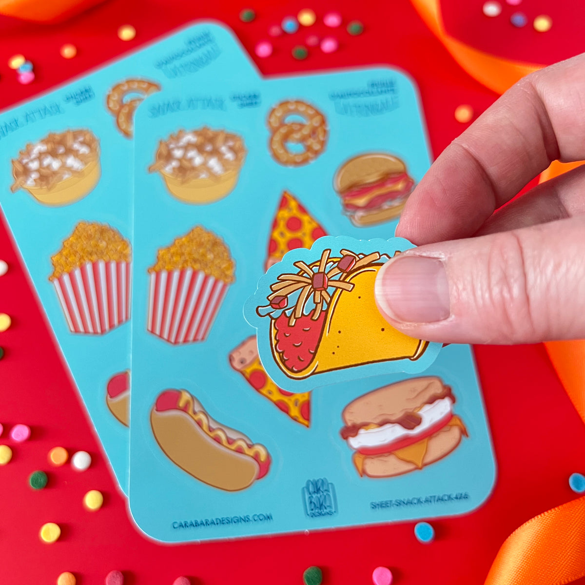 A hand holds a taco sticker peeled from a sticker sheet. The food-themed sticker sheet is in the background.