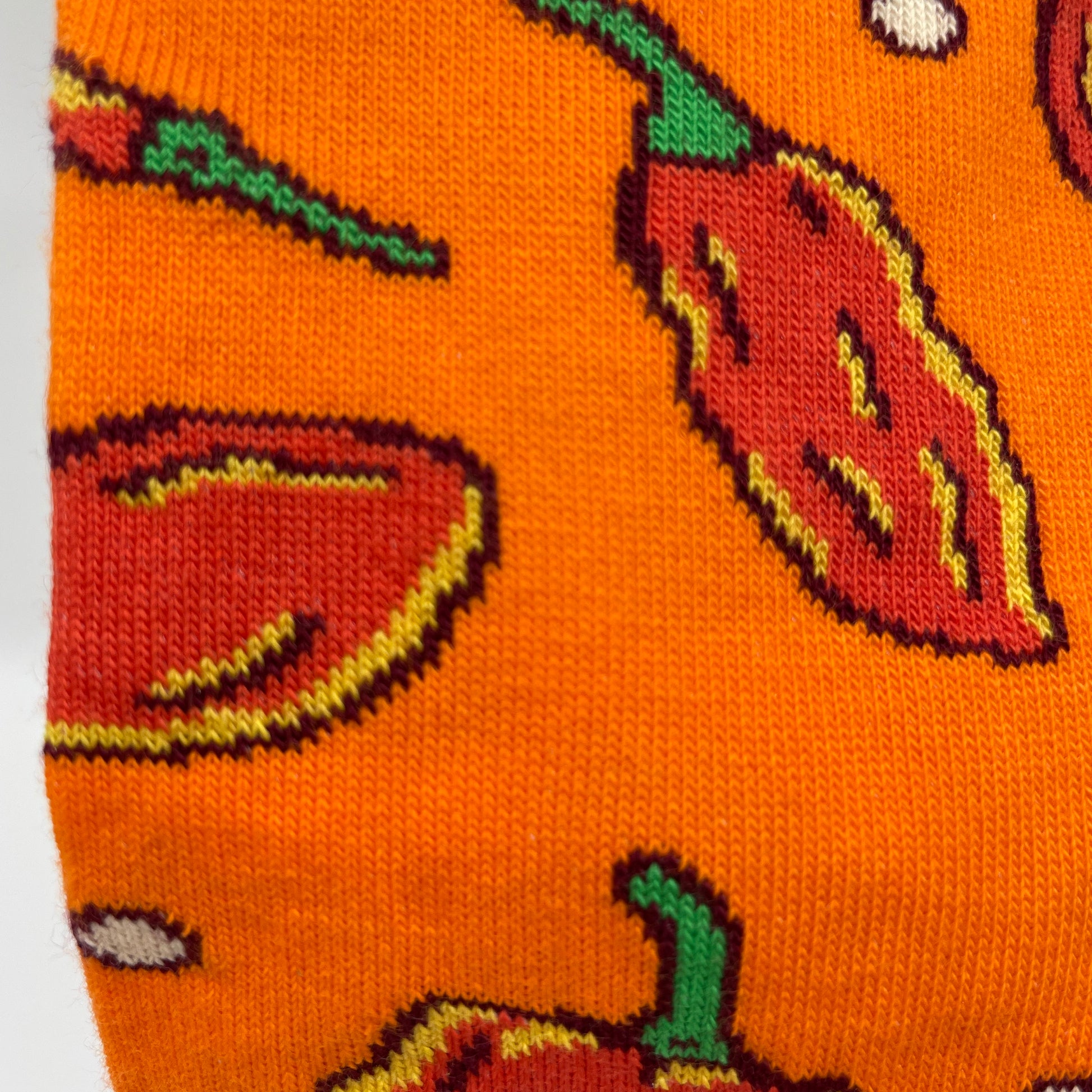 A close-up photo shows detail of a hot pepper pattern woven into an orange organic cotton sock.