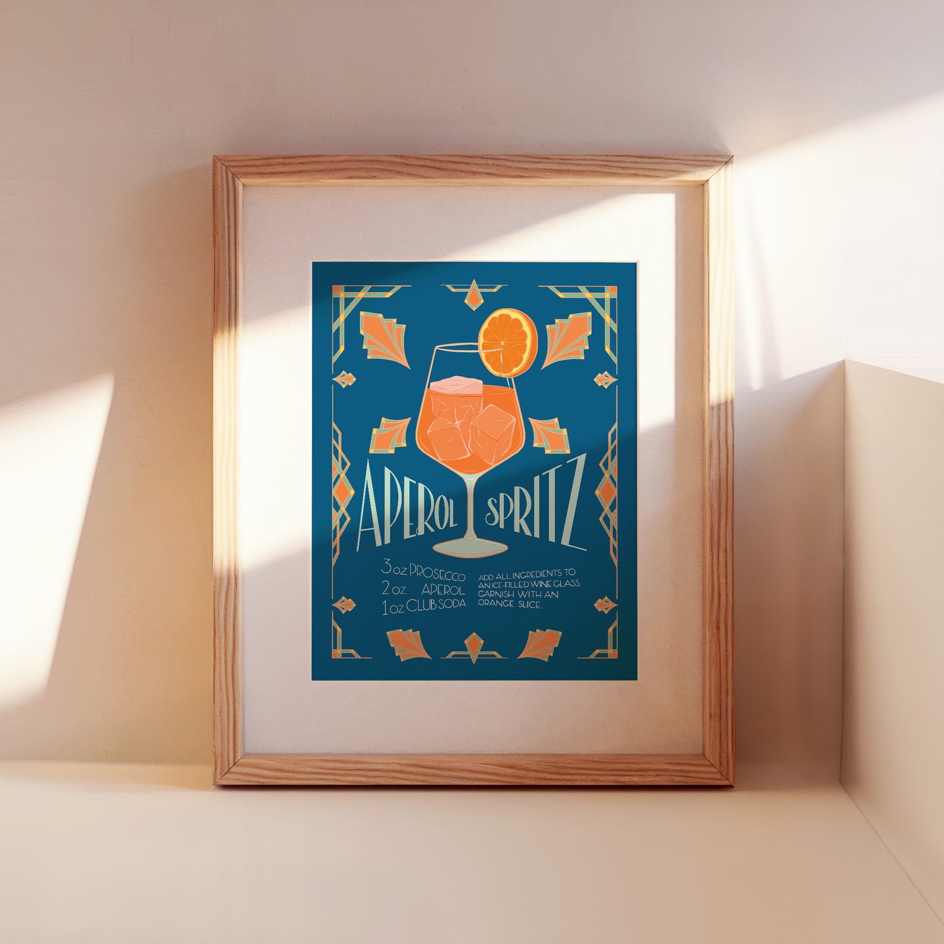 A blue poster of an art deco cocktail recipe for a spritz leans against a wall in a wooden frame.