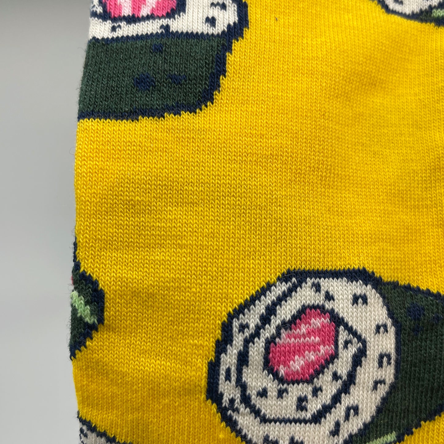 A close-up photo shows detail of a sushi roll pattern woven into a bright yellow organic cotton sock.