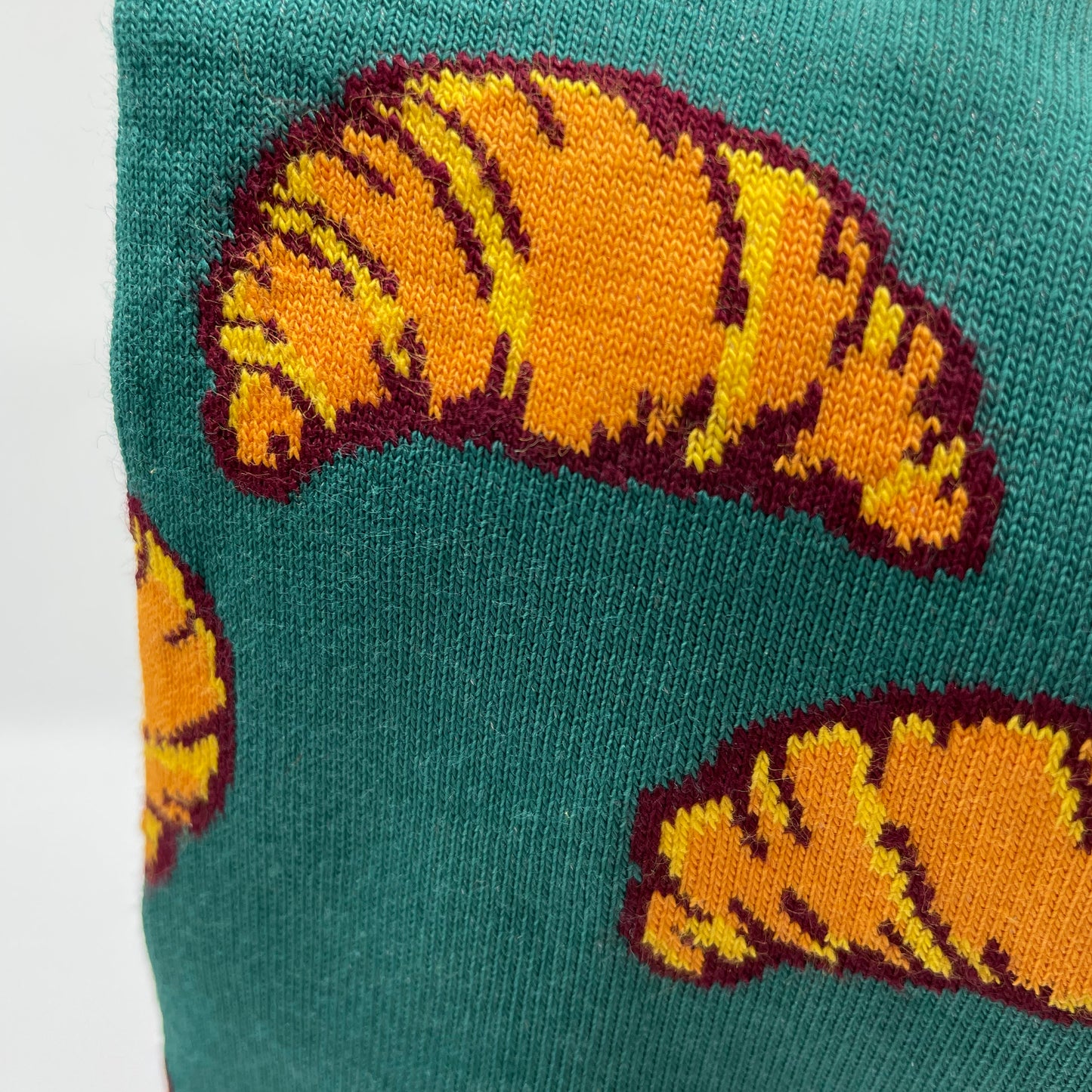 A close-up photo shows a croissant pattern woven into teal organic cotton socks.