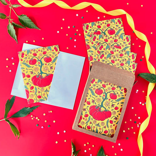 Patterned tomato note cards spill out of a box set. The box is on yellow with confetti, ribbon and leaves.