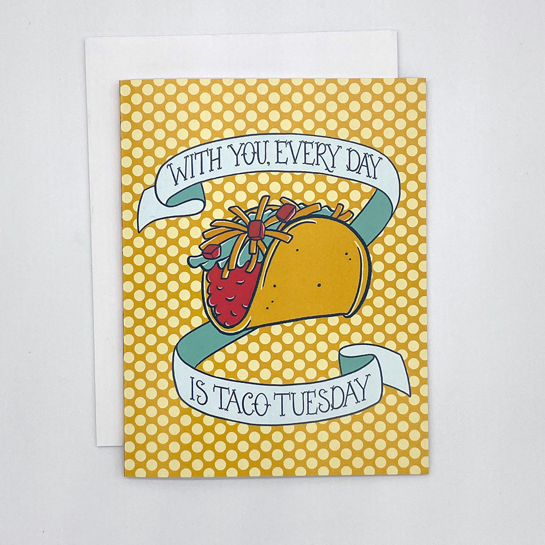 A yellow polka-dot greeting card features an illustration of a hard-shell taco loaded with toppings and the words With You, Every Day is Taco Tuesday in hand-lettering. The card is on a white envelope on a white background.