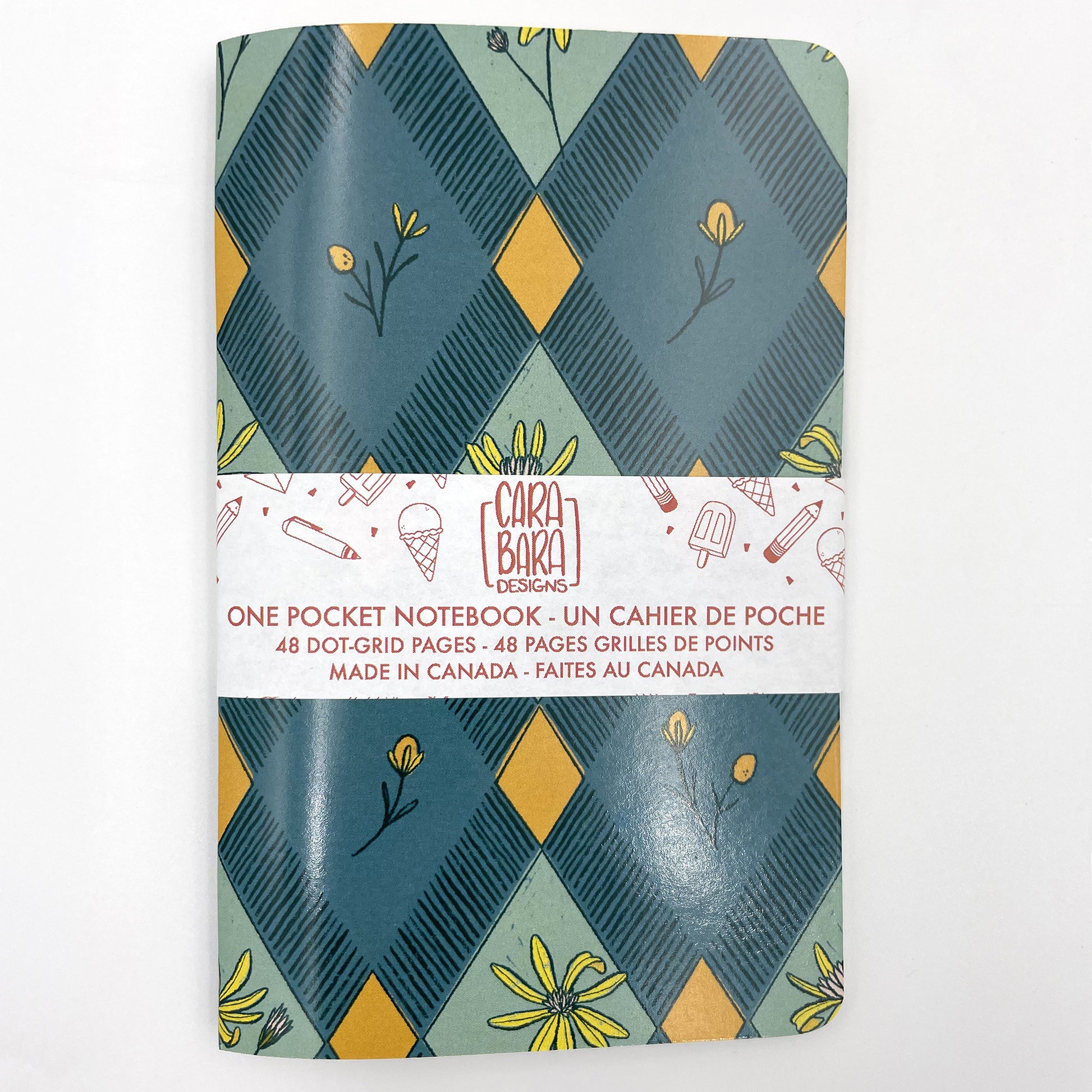 A small closed notebook has a cover that shows a pattern of blue and orange diamonds with wildflowers at the centre of some diamonds. The notebook is bound with a Carabara Designs belly band indicating in both French and English that it is a pocket notebook containing 48 dot grid pages and is made in Canada.