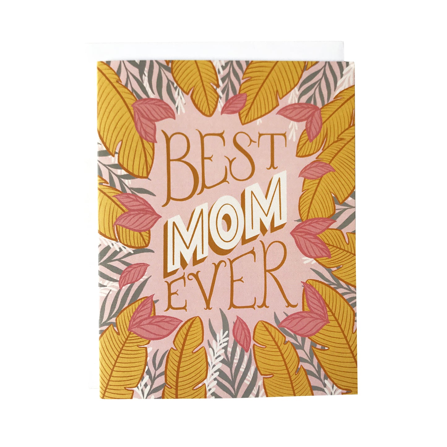 A pink greeting card is covered in golden yellow, white and grey tropical leaves along with the lettered phrase "Best Mom Ever" in block letters. The card sits against a white envelope on a white background.