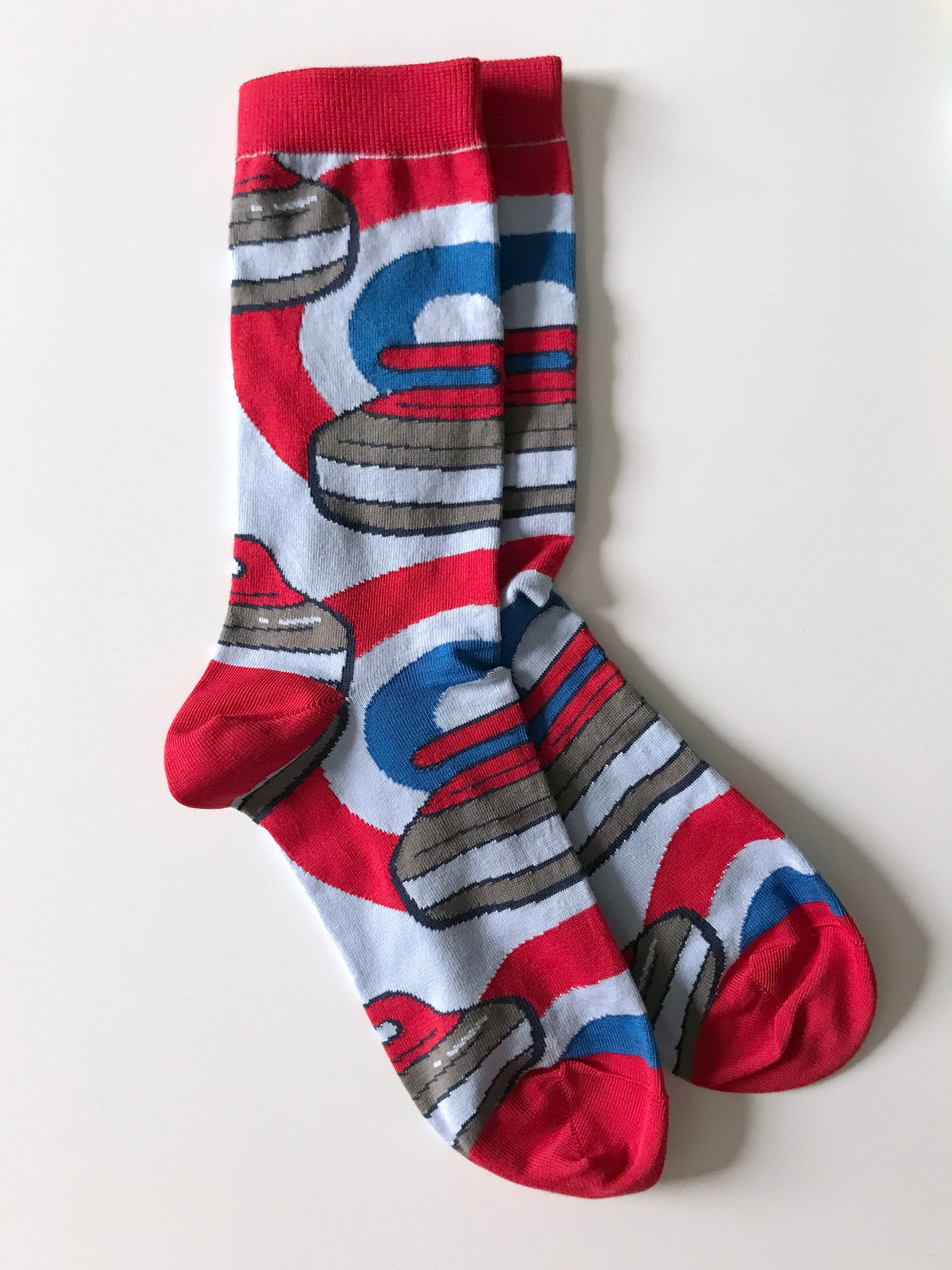 A pair of socks with red cuffs, heels and toes is patterned with curling rocks and red and blue rings.