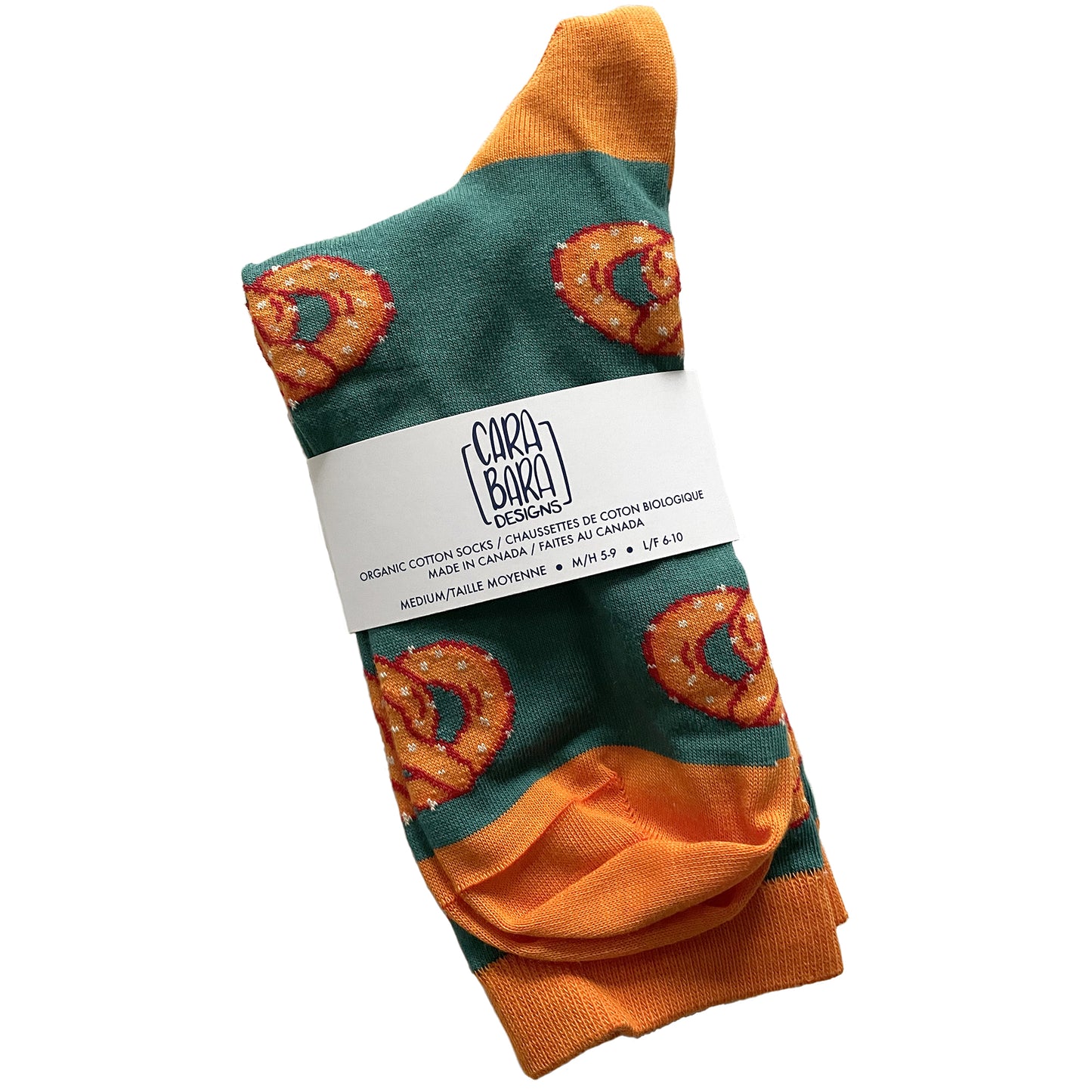 A pair of green socks with orange accents is patterned with orange pretzels and is folded and labelled with a belly band with the Carabara Designs logo and the words organic cotton socks made in Canada, size medium, in English and French.
