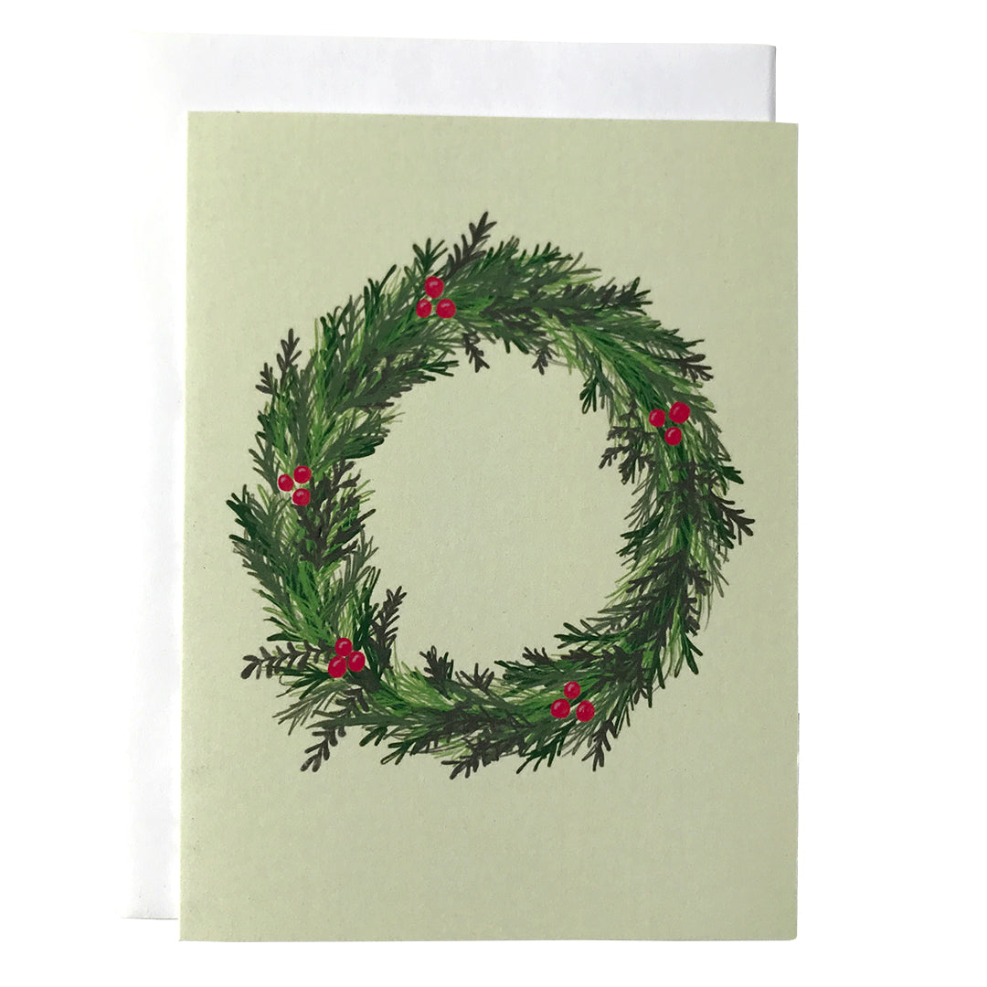 A pale green greeting card is adorned with a wordless illustration of an evergreen wreath adorned by holly berries. The card sits against a white envelope on a white background.